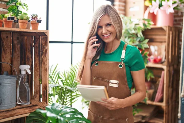 Young Blonde Woman Florist Talking Smartphone Reading Notebook Flower Shop — Stock Photo, Image