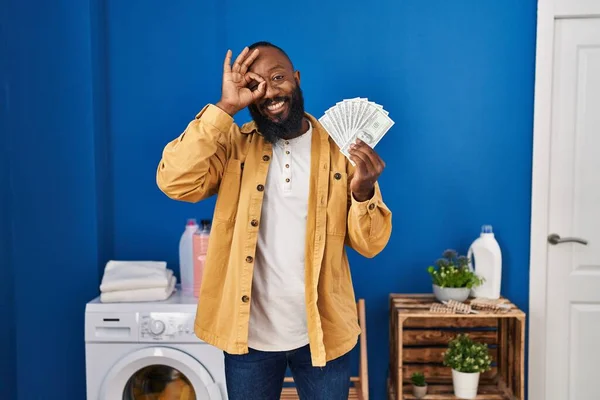 Africký Američan Drží Peníze Prádelně Úsměvem Šťastný Dělá Znamení Rukou — Stock fotografie