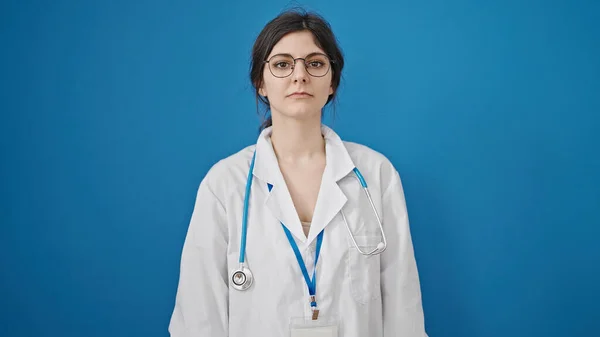 Fiatal Gyönyörű Spanyol Orvos Áll Komoly Kifejezés Izolált Kék Háttér — Stock Fotó