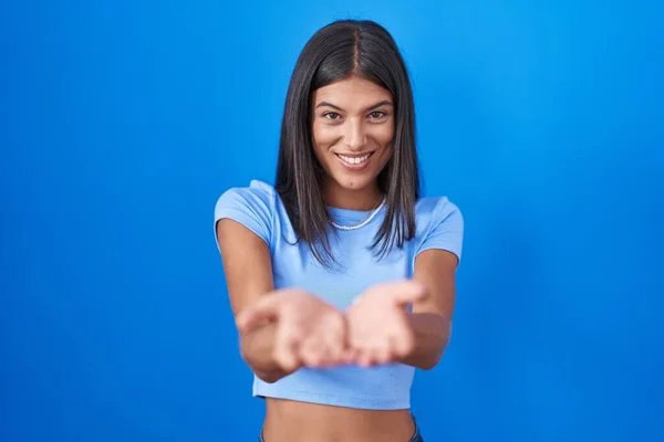 青い背景の上に立っている若い女性が一緒に手の手のひらで笑顔を受信またはジェスチャーを与える 保持し保護する — ストック写真