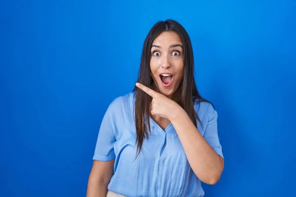 Jonge Brunette Vrouw Staande Blauwe Achtergrond Verrast Wijzend Met Vinger — Stockfoto