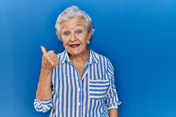 一个白发苍苍的老妇人站在蓝色的背景上 手举着快乐的大拇指做手势 赞成的表情看着相机显示的成功 — 图库照片