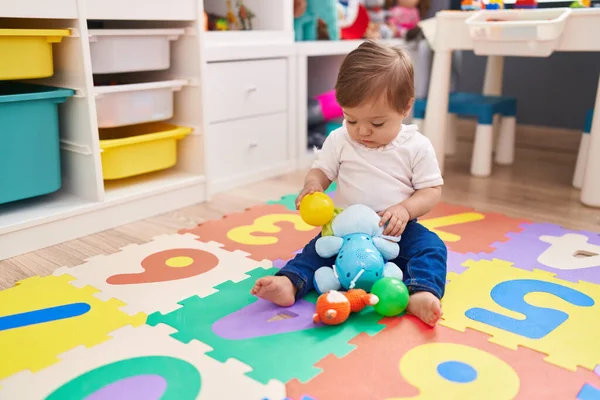 幼稚園の床に座っているボールと象のおもちゃで遊ぶ愛らしい白人の赤ちゃん — ストック写真