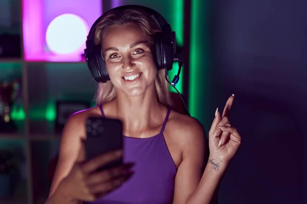 若いですブロンド女性再生ビデオゲームともにスマートフォン笑顔幸せなポインティングとともに手と指へ側 — ストック写真