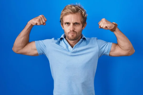 青い背景の上に立っている白人男性は腕の筋肉を誇りに思って笑っている フィットネスのコンセプト — ストック写真