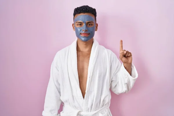 Jovem Hispânico Vestindo Máscara Facial Beleza Roupão Banho Mostrando Apontando — Fotografia de Stock