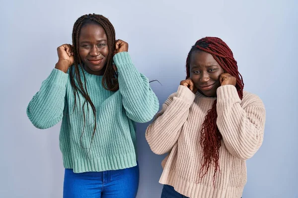 Две Африканки Стоят Синем Фоне Закрывая Уши Пальцами Раздраженным Выражением — стоковое фото
