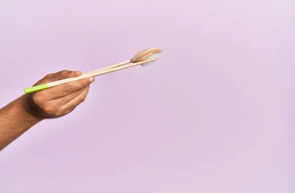 用筷子把黑色扇贝放在孤立的粉色背景上的人的手 — 图库照片