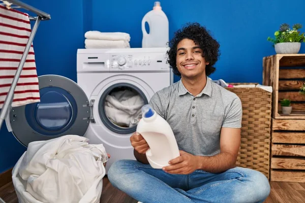 年轻的惊慌失措的男人带着瓶子清洁剂在洗衣房微笑 — 图库照片