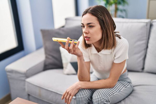 Молодая красивая латиноамериканка разговаривает по смартфону, сидя дома на диване