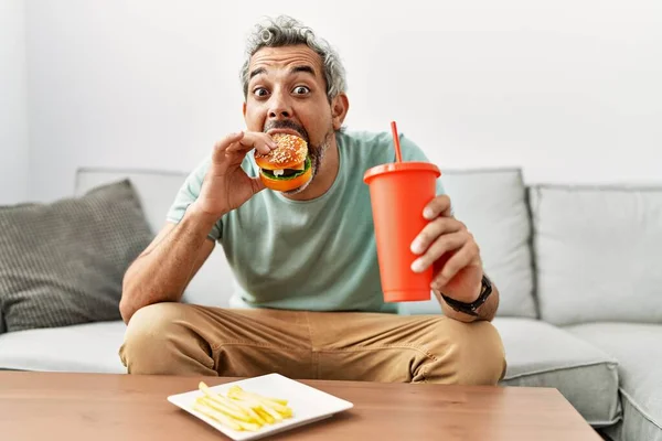 Homem Cabelos Grisalhos Meia Idade Comendo Hambúrguer Sentado Sofá Casa — Fotografia de Stock