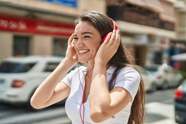 年轻的惊慌失措的女人带着自信的笑容在街上听音乐 — 图库照片