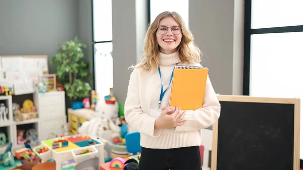 Young Blonde Woman Preschool Teacher Smiling Confident Holding Books Kindergarten — Foto de Stock