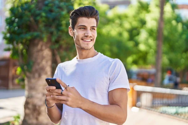 公園でスマートフォンを使って自信を持って笑っている若いヒスパニック系の男 — ストック写真