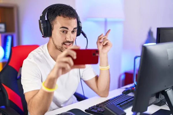 ハンサムなヒスパニック系の男ゲームをプレイしているスマートフォン笑顔幸せなポインティングで手と指で側に — ストック写真