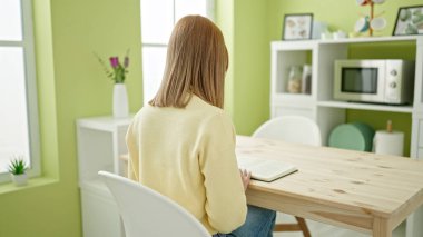 Young blonde woman reading book sitting on table at home