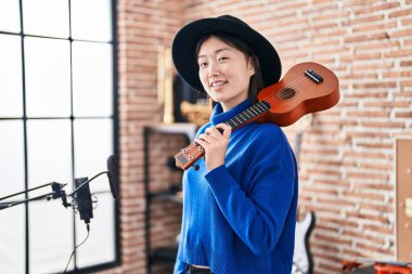 Chinese woman musician smiling confident holding ukulele at music studio