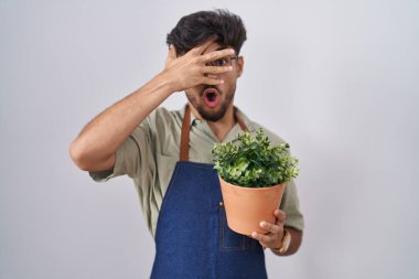 Sakallı, yeşil sakallı bir adam şok içinde yüzünü ve gözlerini kapayarak utangaç bir ifadeyle parmaklarının arasından bakıyor.. 