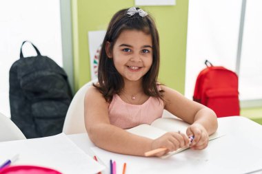 Masada oturan sevimli İspanyol kız öğrenci. Sınıfta kalem açacağı kullanıyor.
