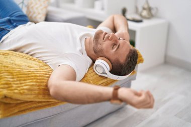 Young caucasian man listening to music lying on sofa at home