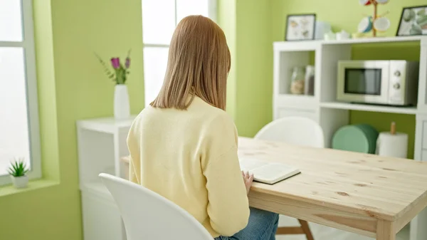 年轻的金发女人坐在家里的桌上看书 — 图库照片