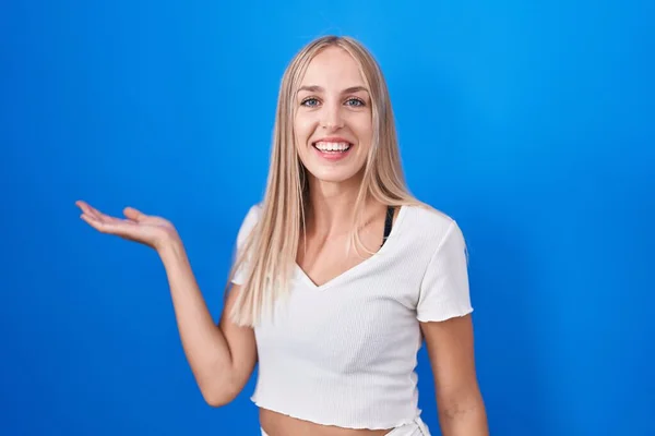 Mladá Běloška Stojí Nad Modrým Pozadím Vesele Usmívá Ukazuje Dlaní — Stock fotografie
