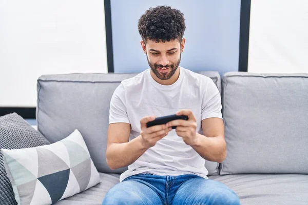 年轻的阿拉伯男子坐在家里的沙发上玩电子游戏 — 图库照片
