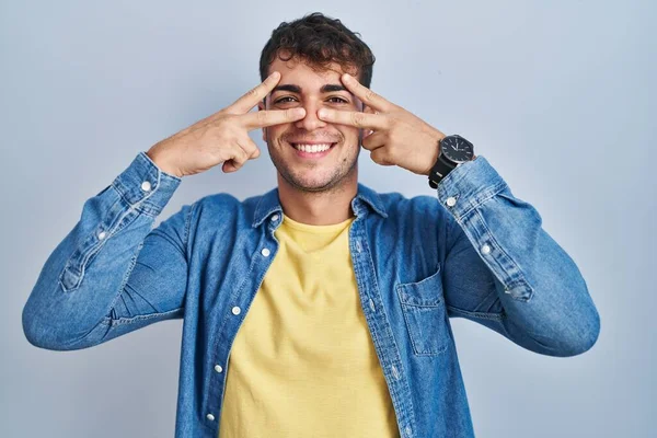 Mladý Hispánec Stojí Nad Modrým Pozadím Dělá Symbol Míru Prsty — Stock fotografie