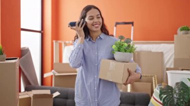 Genç, güzel, İspanyol bir kadın yeni evinde elinde bir kutuyla akıllı telefonuyla sesli mesaj dinliyor.