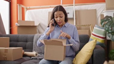 Karton kutuları açan genç, güzel İspanyol kadın telefonda konuşuyor. Yeni evde şikayet ediyor.