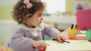 Adorable hispanic girl preschool student sitting on table drawing on paper at kindergarten