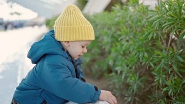 Beyaz çocuk parkta bitkilerle oynarken eğleniyor.