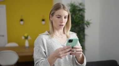 Akıllı telefon kullanan genç sarışın kadın şaşırdı ve evde endişeli.