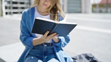 Üniversitede bankta oturmuş kitap okuyan genç sarışın kadın.