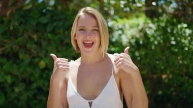 Young blonde woman smiling confident doing ok sign with thumbs up at park