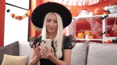 Young blonde woman using smartphone having halloween party at home