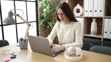 Young beautiful hispanic woman business worker using laptop and headphones working at office