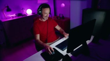 Middle age man streamer playing video game using computer at gaming room