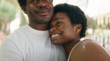 Afro-Amerikalı erkek ve kadın gülümseyen çift parkta birbirlerine sarılıyorlar.