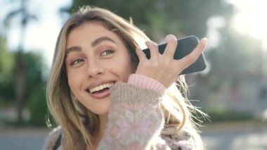 Young blonde woman smiling confident listening audio message by the smartphone at street