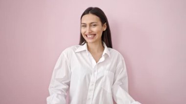 Genç, güzel, İspanyol bir kadın, gülümsüyor. Kendine güveniyor, pembe arka planda dans ediyor.