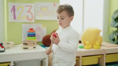 Adorable caucasian boy playing maraca standing at kindergarten