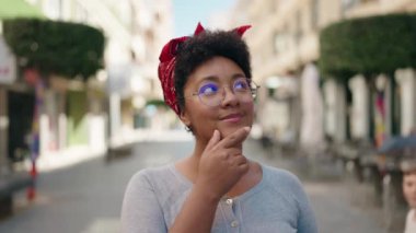 Gözlük takan Afro-Amerikalı kadın sokakta şüpheli bir ifadeyle duruyor.