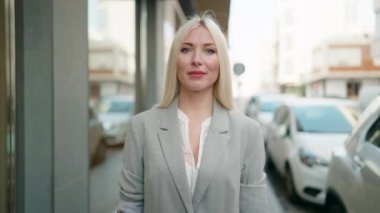 Genç sarışın kadın yönetici gülümseyerek caddede duruyor.