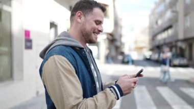 Young caucasian man smiling using smartphone at street
