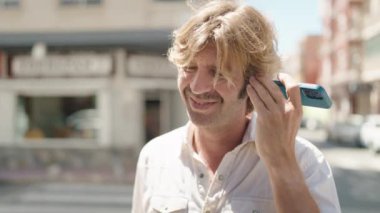 Young man smiling confident listening audio message by the smartphone at street