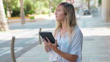 Young blonde woman drawing on touchpad with serious expression at street