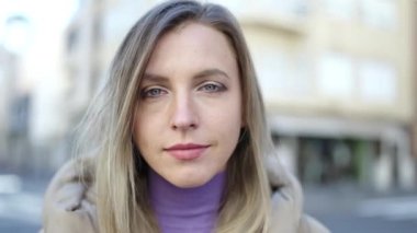 Young blonde woman standing with relaxed expression at street