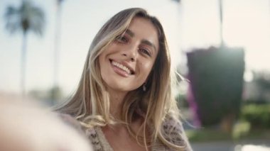 Genç sarışın kadın gülümsüyor. Kendine güveni tam. Sokakta kamerayla selfie çekiyor.
