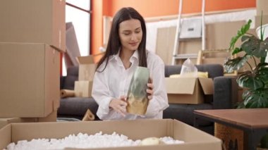 Young beautiful hispanic woman unpacking cardboard box at new home